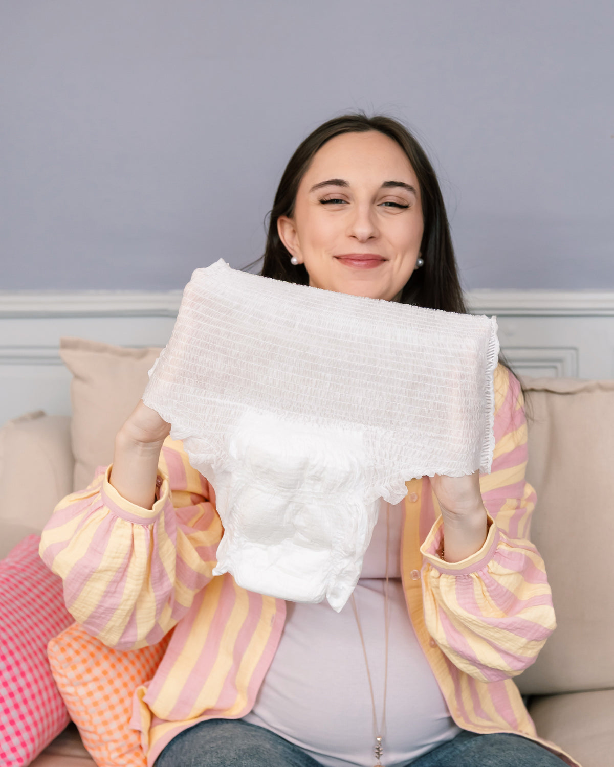 Femme enceinte tenant une culotte jetable post-accouchement Jho déployée — schéma de composition